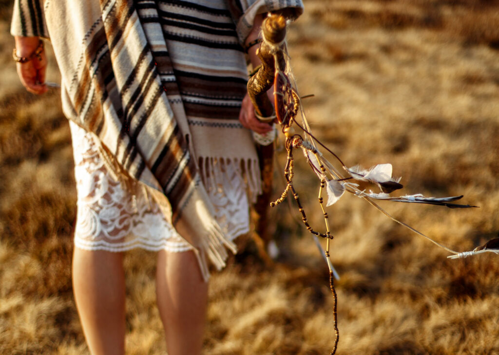 woman legs in native indian american boho dress walking in windy sunny evening mountains, holding feathers